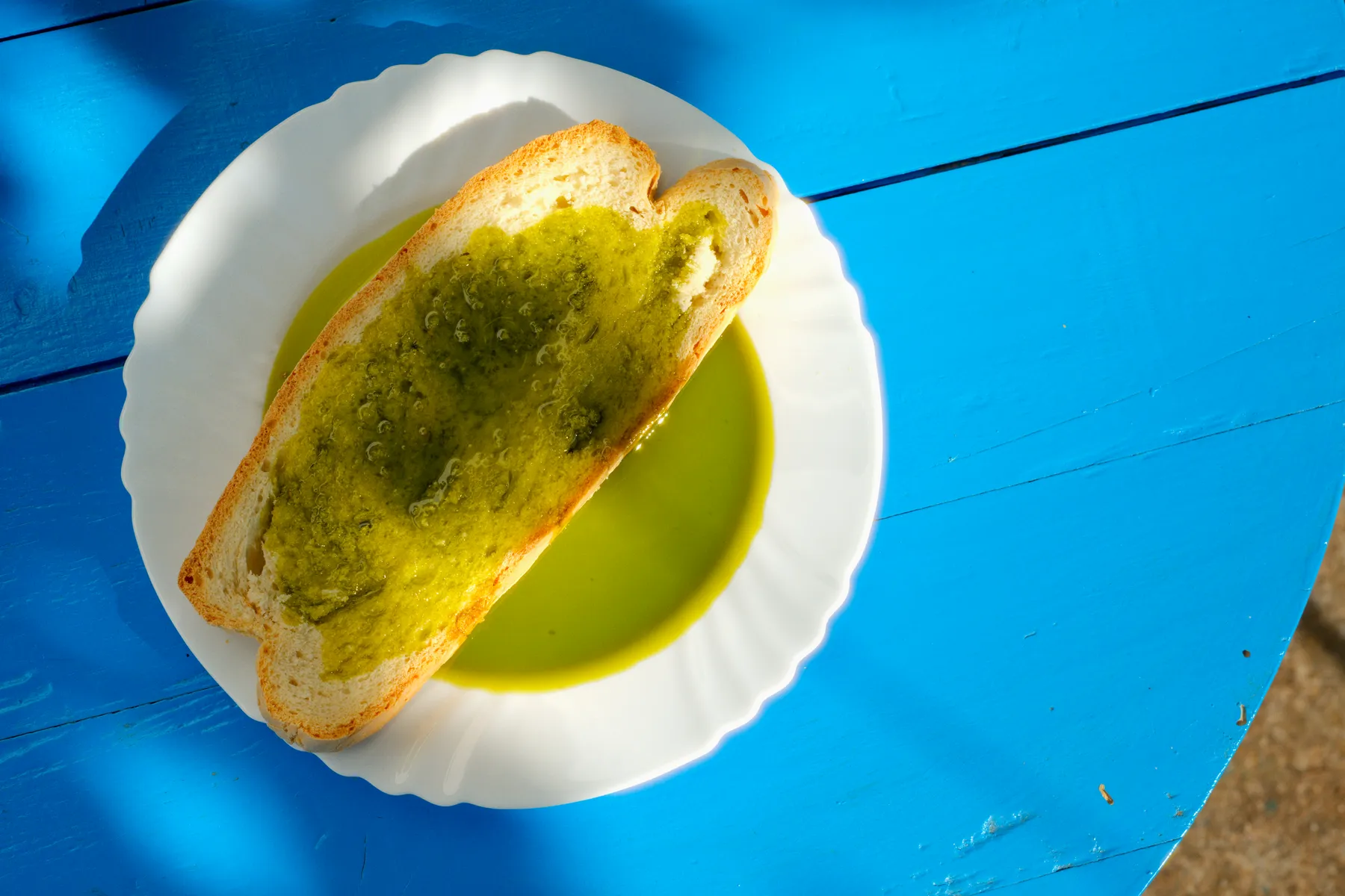 Una tostada mojada en aceite en un plato blanco sobre la mesa azul.