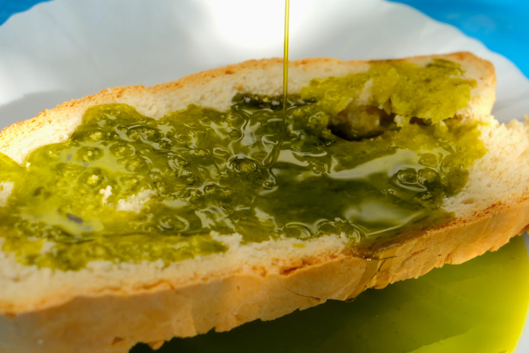 Un hilo de aceite cae sobre una tostada en la mesa azul.